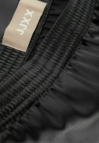Black fabric with a smooth texture, featuring gathered stitching and a tan label with white text, partially visible on the left side.