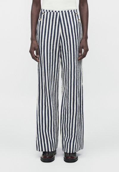 Person wearing high-waist, wide-leg pants with vertical navy and white stripes and black shoes against a plain background.