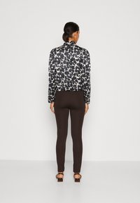 Blusa de estampado en blanco y negro con mangas ajustadas, combinada con leggins marrones. Las sandalias tienen un tacón grueso. Textura de tela suave.