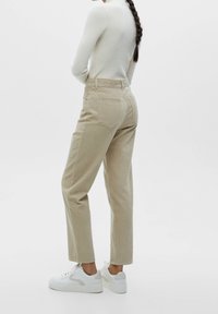 Beige corduroy broek met een hoge taille, rechte pijpen en achterzakken, gecombineerd met witte laag uitgesneden sneakers. Textuurdetail van de stof zichtbaar.