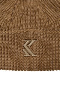 Tan knitted beanie with ribbed texture, featuring a raised beige logo embroidered on the front, providing a structured and snug fit.