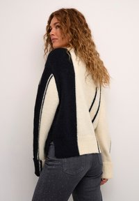 Jersey de punto en crema y marino con rayas diagonales, que cuenta con puños y dobladillo acanalados. Textura suave con un ajuste holgado.