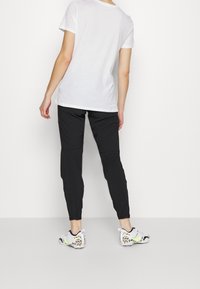 Witte T-shirt met korte mouwen, zwarte taps toelopende broek en ge gedurende sportieve schoenen met een witte basis en kleurrijke accenten, gezien van achteren.