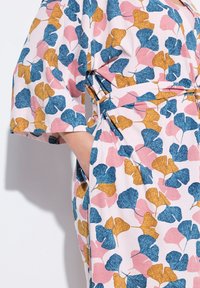 Abito con motivo floreale che presenta foglie di ginkgo blu, rosa e oro su uno sfondo rosa chiaro; include maniche corte e tasche laterali.