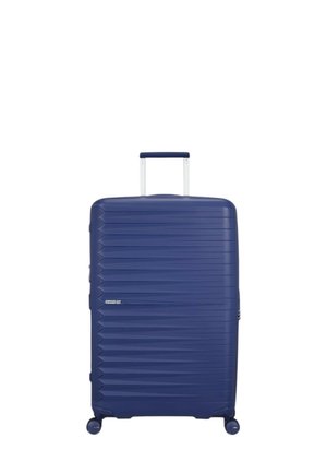 Valise rigide bleu marine avec des lignes diagonales texturées, poignée télescopique argentée et quatre roues pour une mobilité aisée.