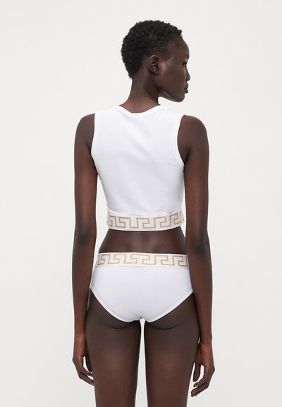 Bílý bavlněný crop top a odpovídající kalhotky s zlatým řeckým klíčovým vzorem podél lemů; přiléhavý design, hladká textura, minimalistický styl.