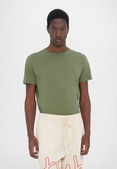 Olive green t-shirt with a round neck, short sleeves, paired with light beige sweatpants featuring red lettering and a textured pattern.