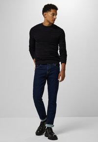 Schwarzer, strukturierter Pullover mit horizontalen Streifen, kombiniert mit dunkelblauen Jeans und schwarzen schnürbaren Stiefeln, mit umgeschlagenen Bündchen.