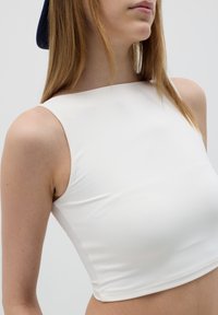 White sleeveless crop top with a square neckline, smooth texture, and fitted design, complemented by neutral background and minimalistic style.