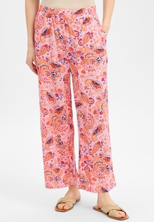 Pantalon de pyjama rose ample avec une taille élastique et un motif paisley floral orange, rouge et violet vif, porté avec des sandales beige à enfiler.