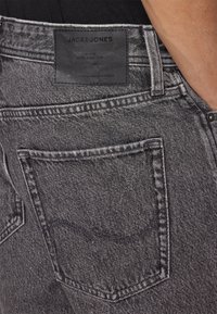 Šedé džíny z denimu s texturovaným povrchem, s malou zadní kapsou a černou koženou nášivkou s razeným textem na pase.