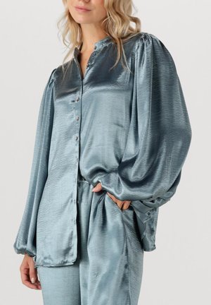 Lichtblauwe satijnen blouse met een knoopsluiting aan de voorkant, lange pofmouwen en een ontspannen pasvorm, met een soepele textuur en een lichte glans.