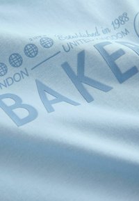 Taevasinine puuvillane T-särk, millel on suur embosseeritud tekst "BAKER" ja väiksem tekst ning maapalli kujundid. Sile tekstuur, lihtne stiil.