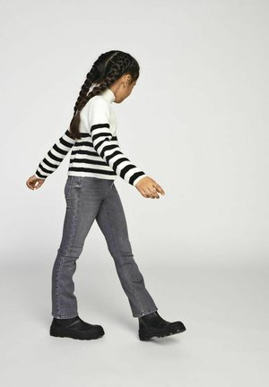 Gestreifter Pullover in Schwarz-Weiß mit langen Ärmeln, kombiniert mit grauen Jeans und schwarzen Stiefeletten. Das Design zeichnet sich durch eine figurnahe Silhouette aus.