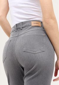 Graue Denim-Jeans mit taillierter Passform, ausgestattet mit einem Lederlabel am Bund und zwei Gesäßtaschen mit sichtbaren Nähten.