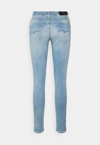 Jeans ajustados en denim de un azul claro, con dos bolsillos traseros que presentan un diseño de puntada en zigzag, una cintura de altura media y una silueta entallada.