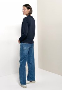 Maglione blu navy con colletto, abbinato a jeans azzurri chiari, larghi. I jeans presentano tasche posteriori e una linea della gamba rilassata.