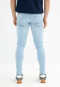 Jeans skinny de color azul claro con dos bolsillos traseros que presentan un patrón de costura en forma de diamante, combinados con zapatillas negras y blancas.