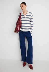 Camiseta polo de manga larga a rayas en blanco y azul marino, combinada con jeans de mezclilla azul de pierna ancha. Bolso rojo brillante y zapatos rojos de punta puntiaguda.