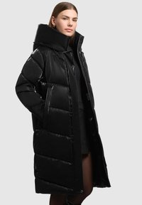 Sort pufferjakke med høj krave, glat overflade og diamantformet polstring. Har lynlås foran og sidelommer.