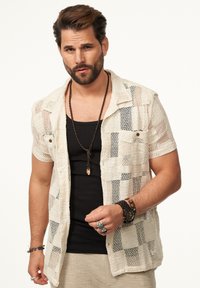 Offenes Strick-Shortsleeve-Shirt in Creme mit einem Karomuster, kombiniert mit einem schwarzen Tanktop. Als Zubehör werden Armbänder und eine Halskette getragen.