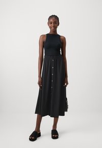 Black ribbed tank top paired with a long black skirt featuring front buttons and an elastic waistband. Black platform slide sandals.