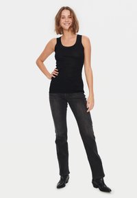 Melna bezmugura topa krekls ar pieguļošu dizainu un platiem plecu siksnām, apvienots ar tumšu džinsu biksēm. Modelis stāv ar rokām uz gurniem, tērpts melnās augstpapēžu kurpēs.