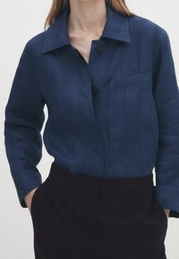 Donkerblauw overhemd met kraag, een enkele borstzak en lange mouwen. Gemaakt van een gestructureerde stof. Combinatie met donkere broeken.