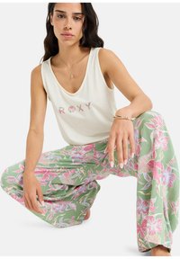 Licht crèmekleurig tanktop met "ROXY" in bloemmotief; losse, geprinte groene broek met roze tropisch bloemdesign; zacht materiaal, ontspannen pasvorm.
