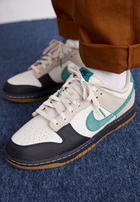 Boty Nike s krémovým svrškem, černou špičkou, tyrkysovými akcenty a šedými semišovými detaily; pryžová podrážka s kontrastním sešitím.