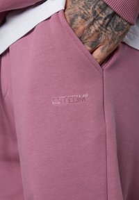 Pink cotton pants with a pocket, featuring an embossed logo "ESTEEM." Soft texture and relaxed fit with ribbed detailing at the waistband.