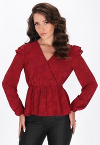 Rote Bluse mit Blumenmuster, langen Ärmeln, rüschigen Schulterakzenten, einem V-Ausschnitt und einem elastischen Taillenbund. Der Stoff hat ein strukturiertes Muster.