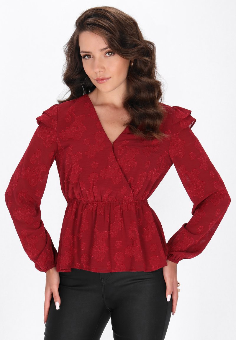 Rote Bluse mit Blumenmuster, langen Ärmeln, rüschigen Schulterakzenten, einem V-Ausschnitt und einem elastischen Taillenbund. Der Stoff hat ein strukturiertes Muster.