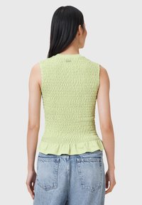 Ljusgrön, ärmlös topp med smockad textur och volang nertill, i kombination med högmidjade blå denimjeans.