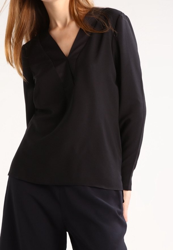 Top a maniche lunghe nera con scollo a V, realizzato in tessuto morbido, caratterizzato da una vestibilità rilassata e uno stile minimalista. Nessun motivo o accessorio visibile.