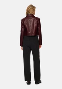 Burgundy leather cropped jacket with a notched collar, paired with black trousers. The jacket features a smooth texture and minimal detailing.