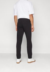 Zwarte broeken met een tapered fit, elastische tailleband en een achterzak. Draag het met een wit t-shirt en witte sneakers met beige zolen.