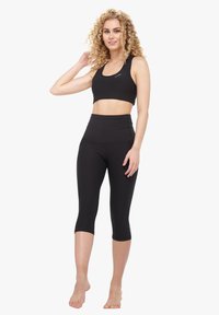 Schwarzes sportliches Crop-Top und hochgeschnittene Leggings aus dehnbarem Material. Das Top hat einen runden Ausschnitt; die Leggings haben eine glatte Oberfläche.