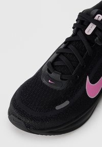 Ingrandimento di una scarpa da corsa nera Nike con swoosh e lacci rosa su sfondo bianco.