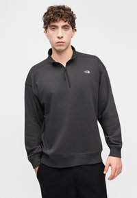 Σκούρο γκρι φούτερ κατασκευασμένο από μαλακό ύφασμα, με γιακά με μισό φερμουάρ και μικρό λογότυπο στο στήθος, με ριμπ μανσέτες και τελείωμα.