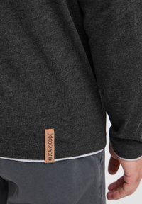Donkergrijze lange mouwen shirt met een gestructureerd materiaal, contrasterende witte zoom en een merknaam leren label in bruin nabij de onderkant.