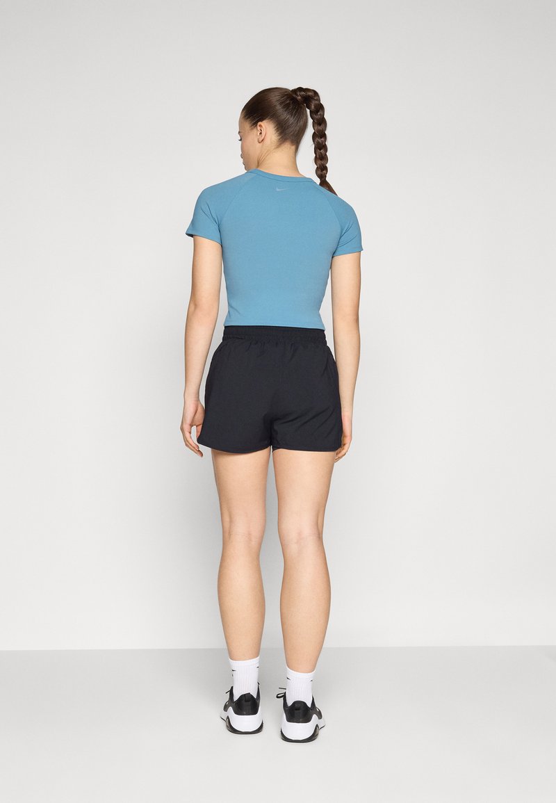 Top azul ajustado de manga corta con escote redondo y pantalones cortos deportivos negros. El conjunto se completa con calcetines blancos y zapatillas deportivas negras.