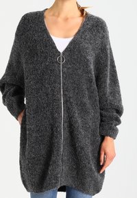 Kolsvart, fluffig oversized cardigan med V-ringning, framdragkedja och långa ärmar. Mjuk textur med avslappnad passform.