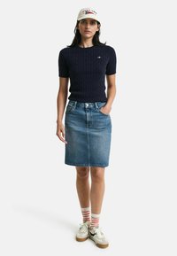 Marine kabelgebreide korte mouwen trui, lichtblauwe denim kokerrok, crèmekleurige pet met rode en blauwe tekst, gestreepte sokken en sneakers.