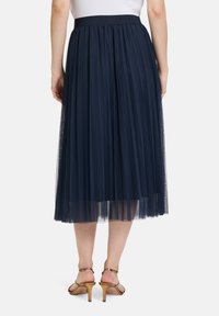 Marineblauwe geplooide tule midi-rok met een elastische tailleband, gecombineerd met tan hoge sandalen. De doorschijnende textuur accentueert het gelaagde ontwerp.