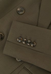 Rudos spalvos pritaikyto stiliaus švarko rankovė ir priekinė dalis su keturiais tokios pačios spalvos mygtukais ant rankogalių ir dviem mygtukais priekyje, lygios tekstūros audinys.