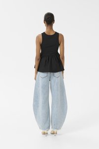 Top peplum nero con corpo fitted e fondo a campana, abbinato a jeans in denim oversize blu chiaro con orli strappati.