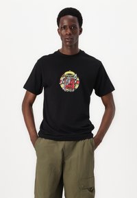 Black cotton t-shirt featuring a colorful graphic of a skeleton in a red outfit with a yellow sombrero, set against a circular backdrop.