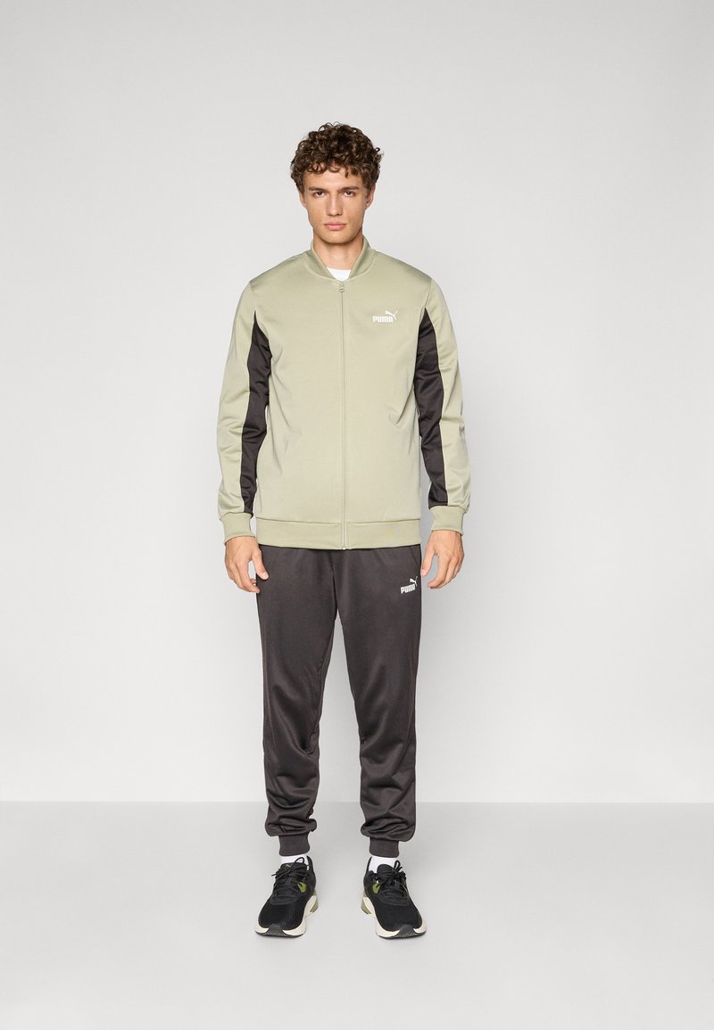 Trackjakke i lys grøn med sorte ærmer, lynlåsåbning og logo. Kombineret med matchende mørke bukser og sorte sneakers. Glat stof.
