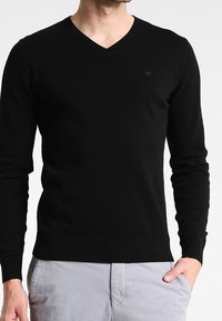 Svart v-halsad tröja i mjukt material med långa ärmar, med ribbad nederkant och muddar, samt en liten logotyp på övre vänstra bröstet.